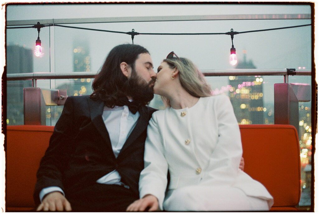 NYC elopement photographer captures couple in black tie and white suit drinking martinis on a rooftop at sunset, shot on film.