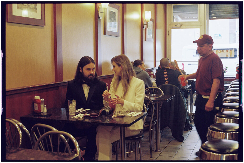 NYC elopement photographer captures bride and groom in diner sharing pancakes for their wedding dinner, candid film photography.