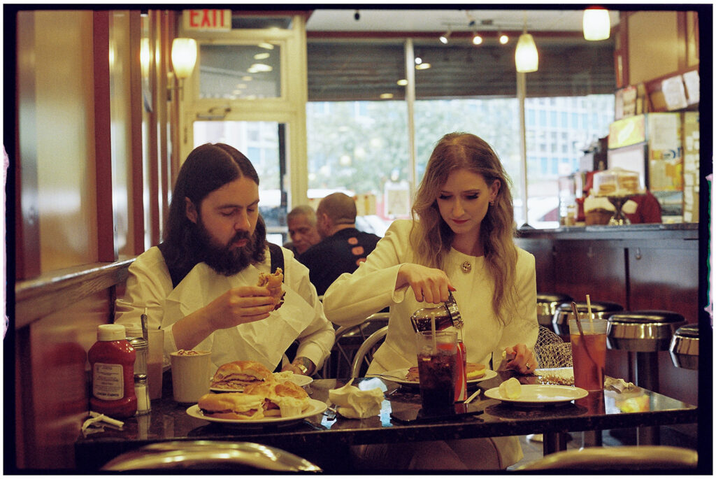 NYC elopement photographer captures bride and groom in diner sharing pancakes for their wedding dinner, candid film photography.
