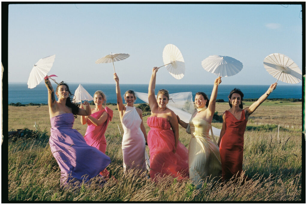 Bride and bridesmaids in colourful dresses posing by vintage car, Kinkell Byre wedding shot on film