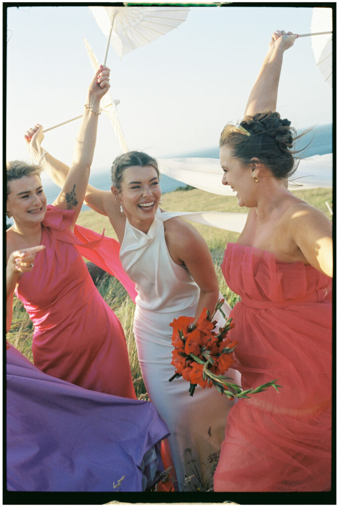 Bride and bridesmaids in colourful dresses posing by vintage car, Kinkell Byre wedding shot on film