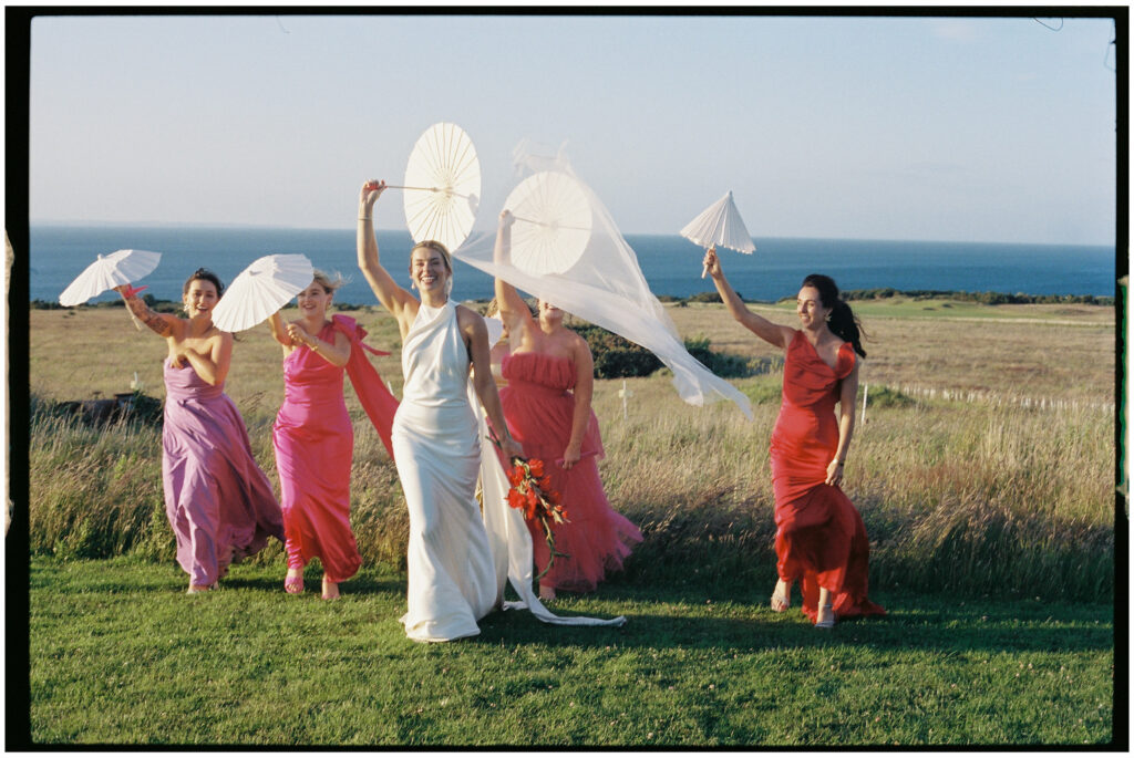 Bride and bridesmaids in colourful dresses posing with parasols at Kinkell Byre wedding shot on film
