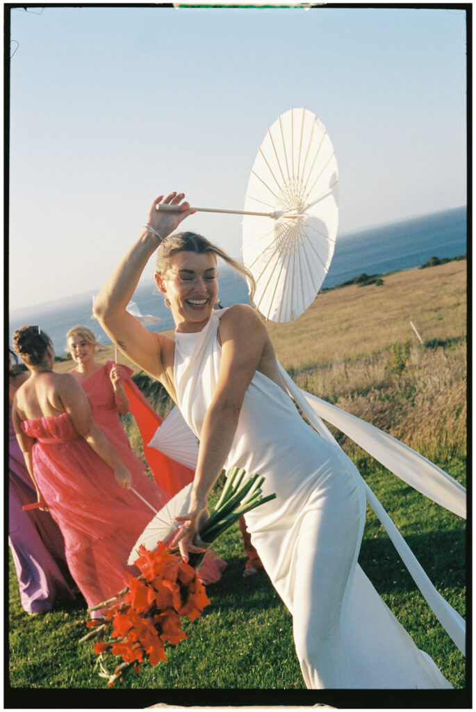 Bride and bridesmaids in colourful dresses posing with parasols at Kinkell Byre wedding shot on film