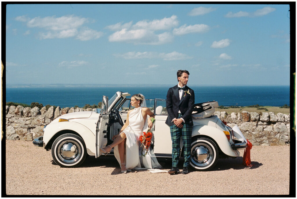 Bride and groom leaning on white classic car with sea view, film wedding photographer Scotland