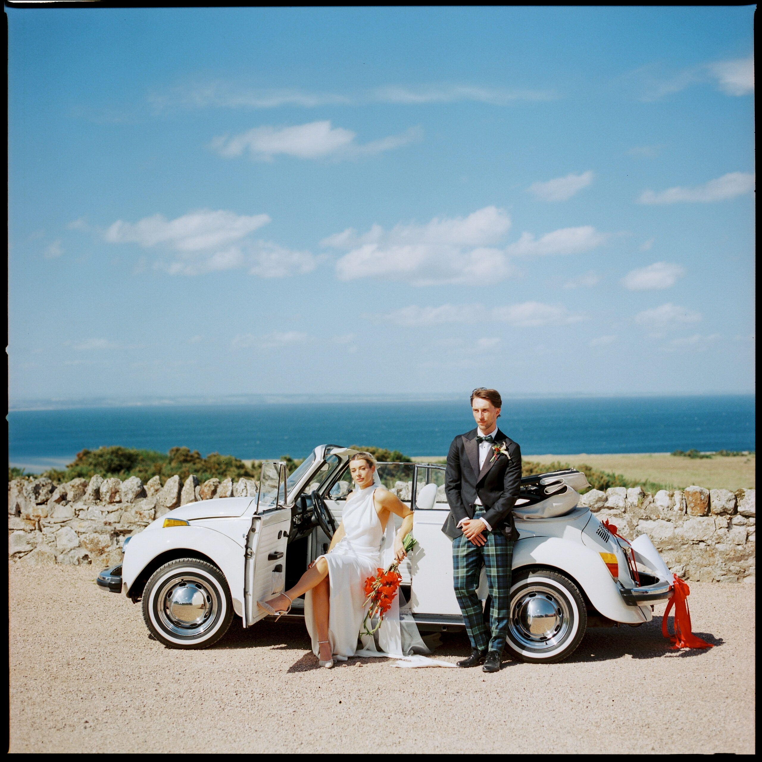 Bride and groom leaning on white classic car with sea view, film wedding photographer Scotland