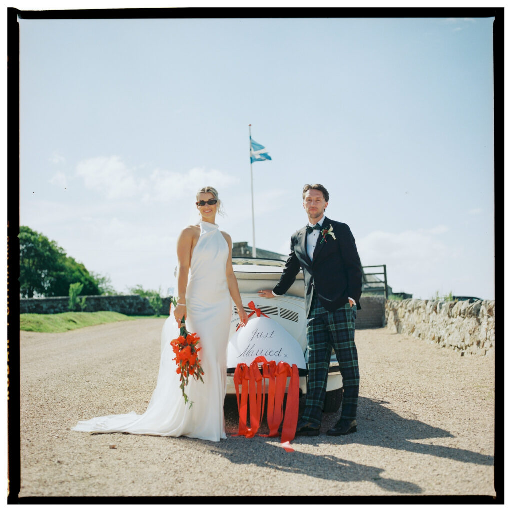 Bride and groom leaning on white classic car with sea view, film wedding photographer Scotland